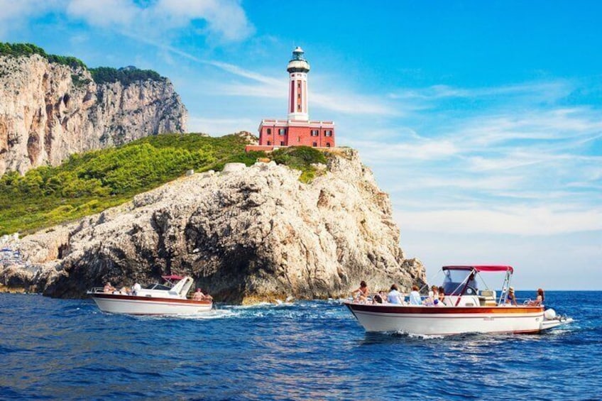 Paesaggio costiero con un faro su una scogliera rocciosa, due imbarcazioni sull'acqua e cielo sereno. 1