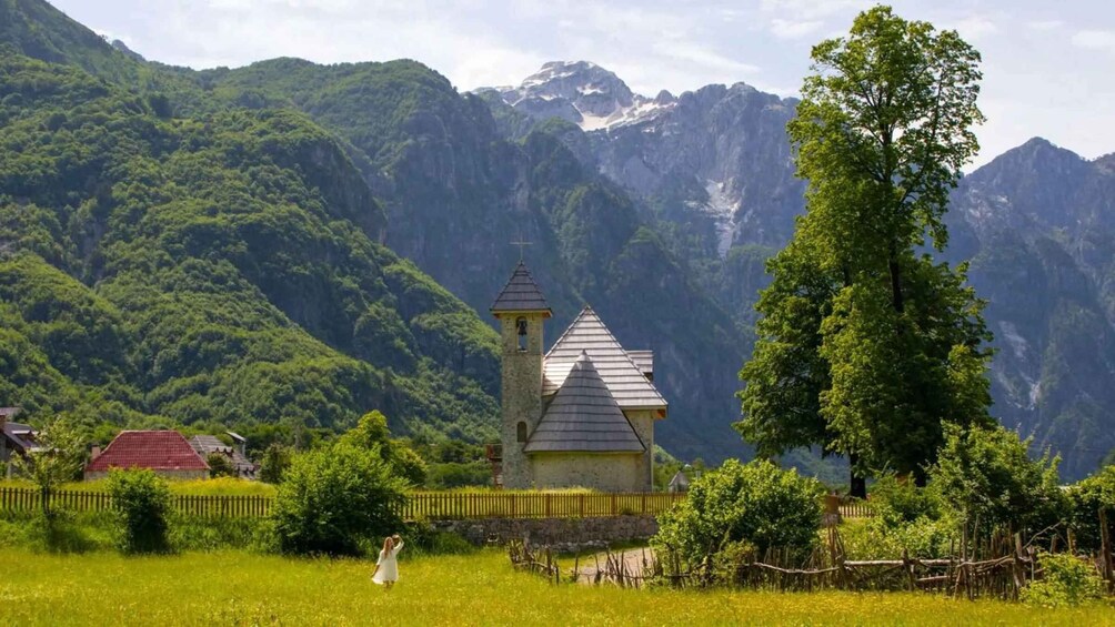 A church with a bell tower in a mountainous area with lush greenery and a person in a white dress. 2