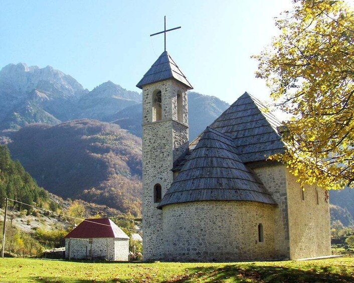 A church with a bell tower and a smaller building, surrounded by mountains and autumn foliage. 3