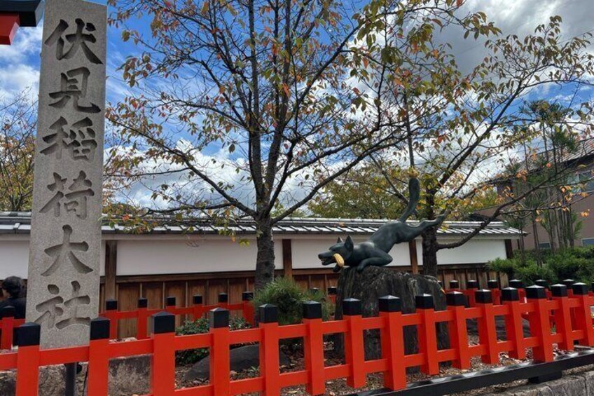 Ein traditionelles japanisches Gebäude mit rotem Zaun, einem Steinmonument mit japanischen Schriftzeichen und einem Baum mit Herbstlaub. 3