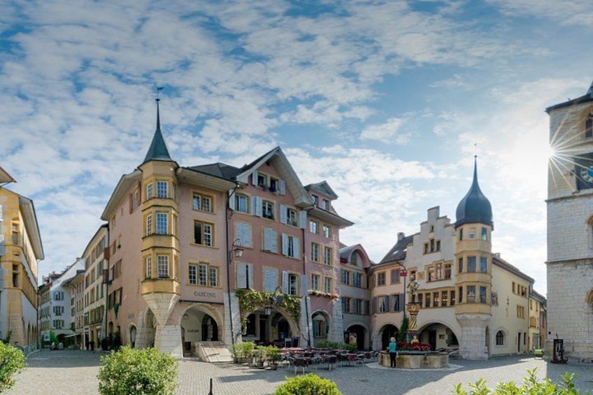 A historic European town square with colorful buildings, a fountain, and a clock tower. 3