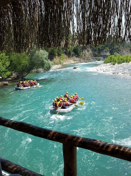 Two groups of people rafting down a turquoise river surrounded by greenery. 2