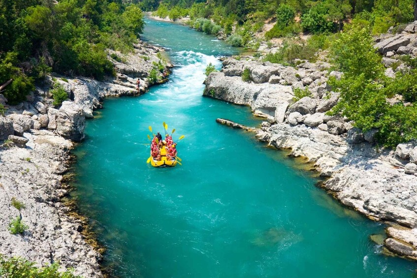 A group of people rafting down a turquoise river surrounded by rocky terrain and greenery. 5