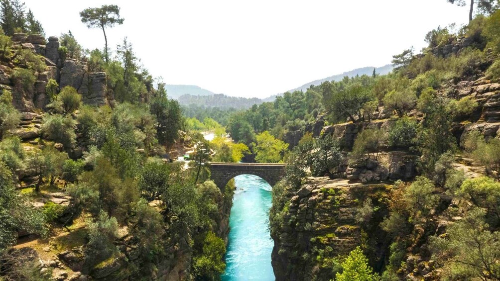 A canyon with a bridge over a turquoise river, surrounded by rocky cliffs and dense greenery. 3