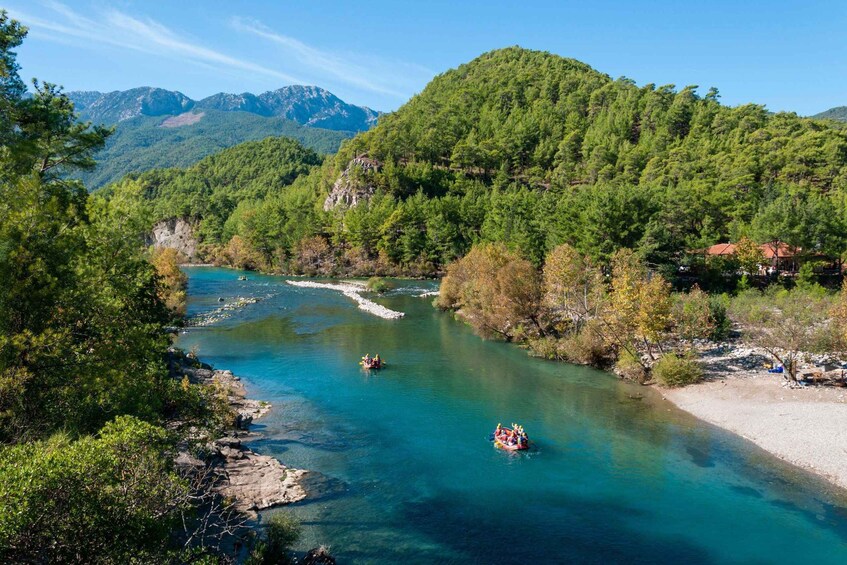 A river with clear water, surrounded by dense green forest and mountains in the background. 1