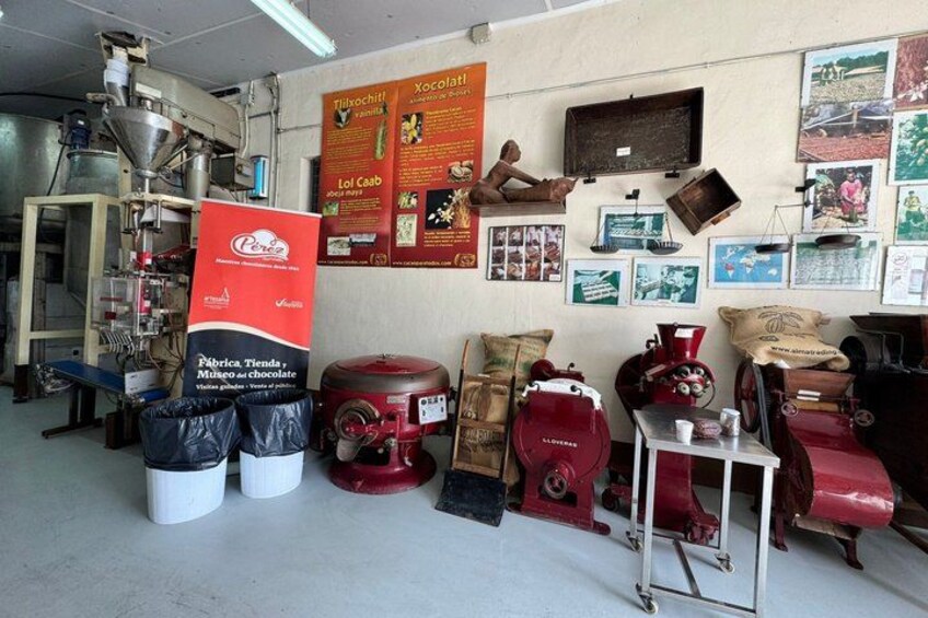 Interno di una fabbrica di cioccolato con macchinari, sacchi di cacao e manifesti pubblicitari. 1