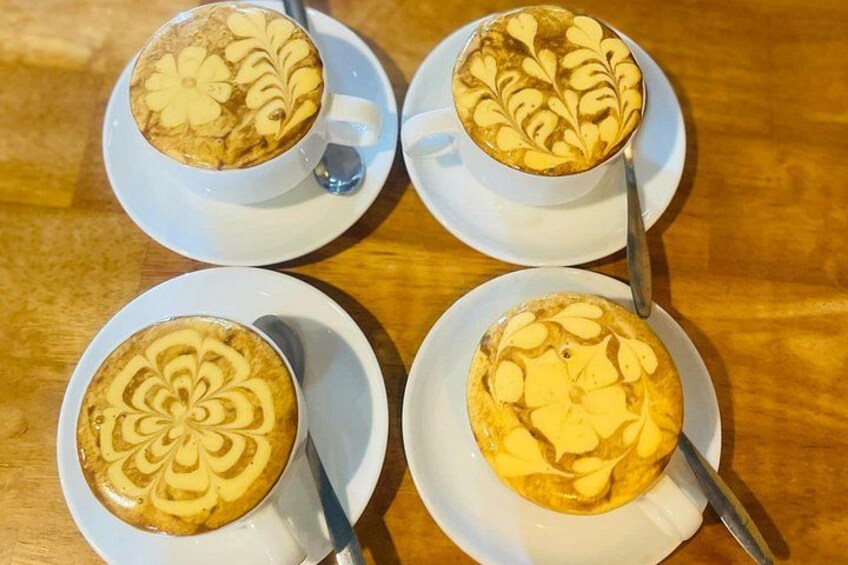 Quatre tasses de café décorées de motifs en latte, posées sur une table en bois. 1