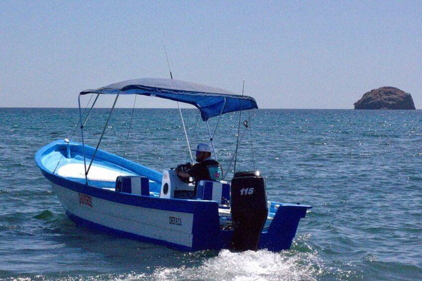 Un barco a motor azul y blanco con toldo, navegando sobre aguas tranquilas con una pequeña isla al fondo. 4