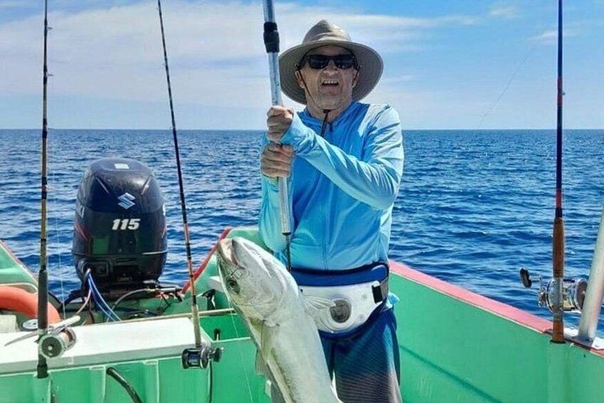Una persona en un bote con motor, sosteniendo una caña de pescar, con el océano al fondo. 2