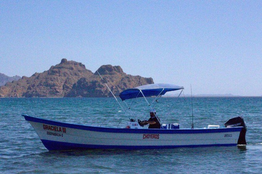 Un barco llamado 'GRACIELA III' con toldo azul, navegando sobre aguas tranquilas con una isla rocosa al fondo. 1