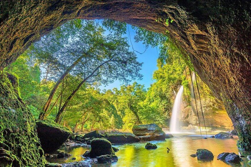 Entrada a una cueva con cascada, rodeada de exuberante vegetación y rocas. 1