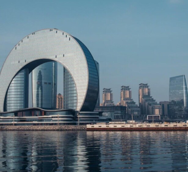 Una estructura arquitectónica moderna con un diseño circular grande, una masa de agua en primer plano y el horizonte de una ciudad al fondo. 4