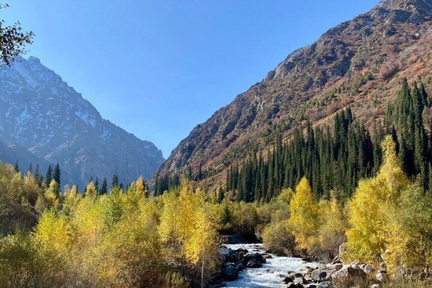 A river flowing through a mountainous area with autumn-colored trees and a clear blue sky. 4