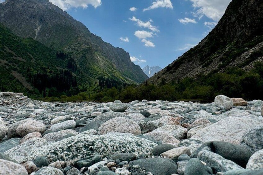 A river with large rocks, mountains, and a clear sky. 1