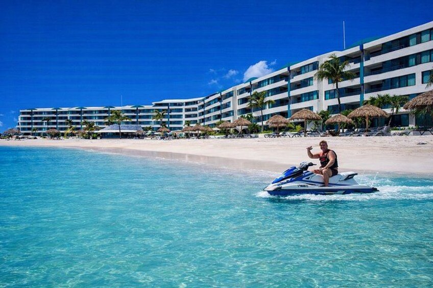 A person jet-skiing on clear turquoise water with a resort in the background. 1