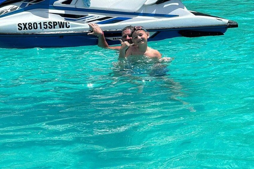 A person swimming in clear blue water with a jet ski in the background. 4