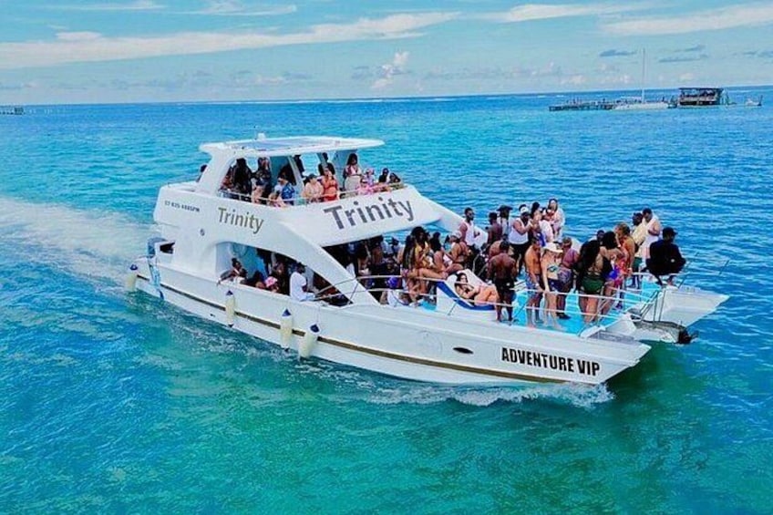 A white boat named 'Trinity' with 'Adventure VIP' written on the side, floating on clear blue water. 2