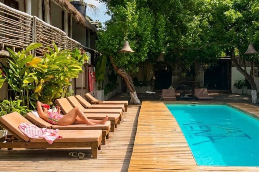 Una terraza de madera con sillones de descanso, una piscina y vegetación tropical. 2