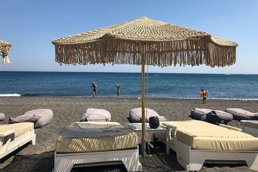Ein Strand mit Liegestühlen, einem Strohdachschirm und dem Meer im Hintergrund. 2