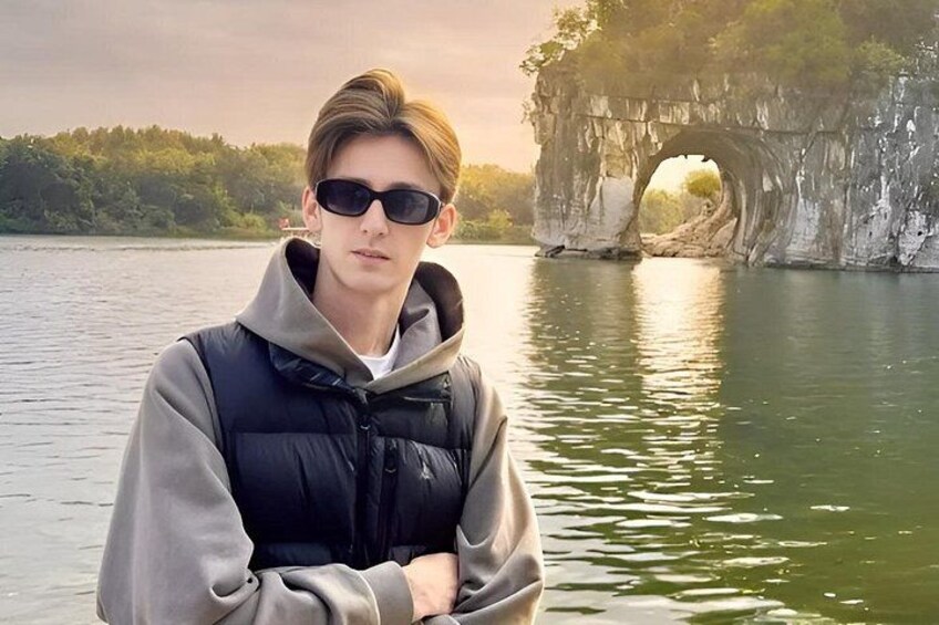 A person standing by a lake with a natural rock formation in the background. 1