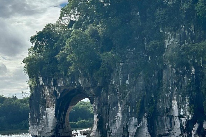 A natural rock formation with a large archway, surrounded by dense greenery and trees. 3