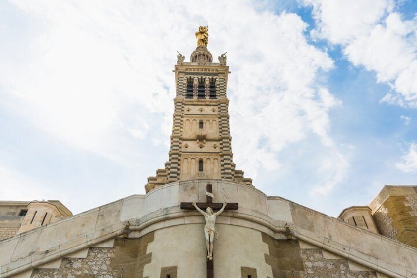 A tower with a statue on top, a cross at the base, and a clear sky. 5