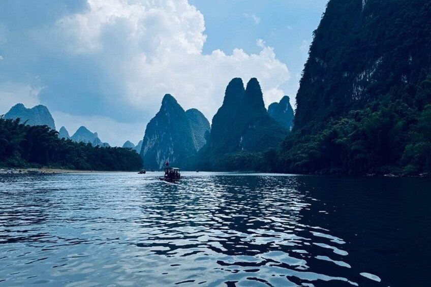 Une rivière paisible où une barque flotte, entourée de hautes montagnes escarpées et d’une végétation luxuriante. 4