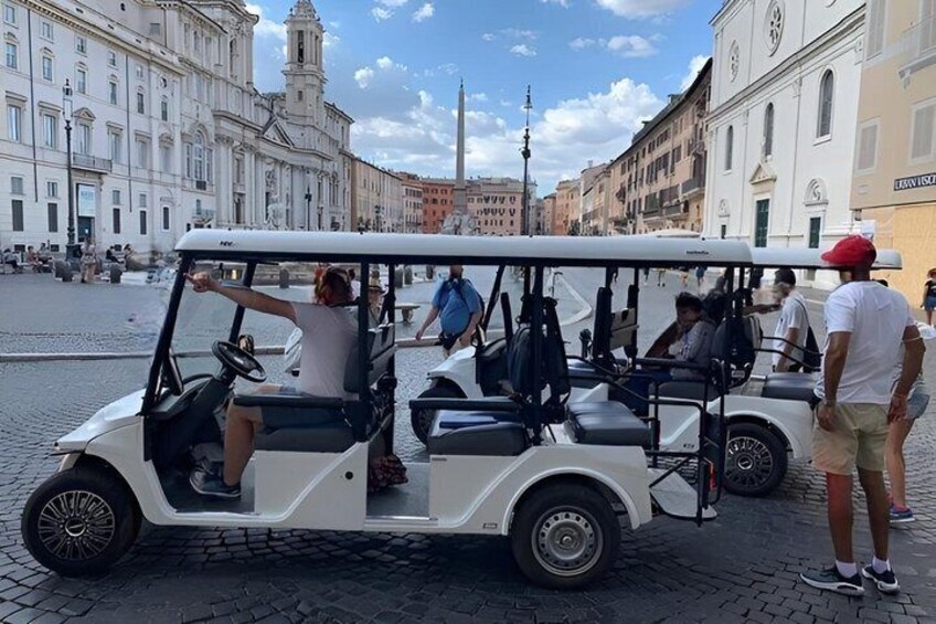 Un carrito de golf blanco estacionado en una calle empedrada con turistas. 5
