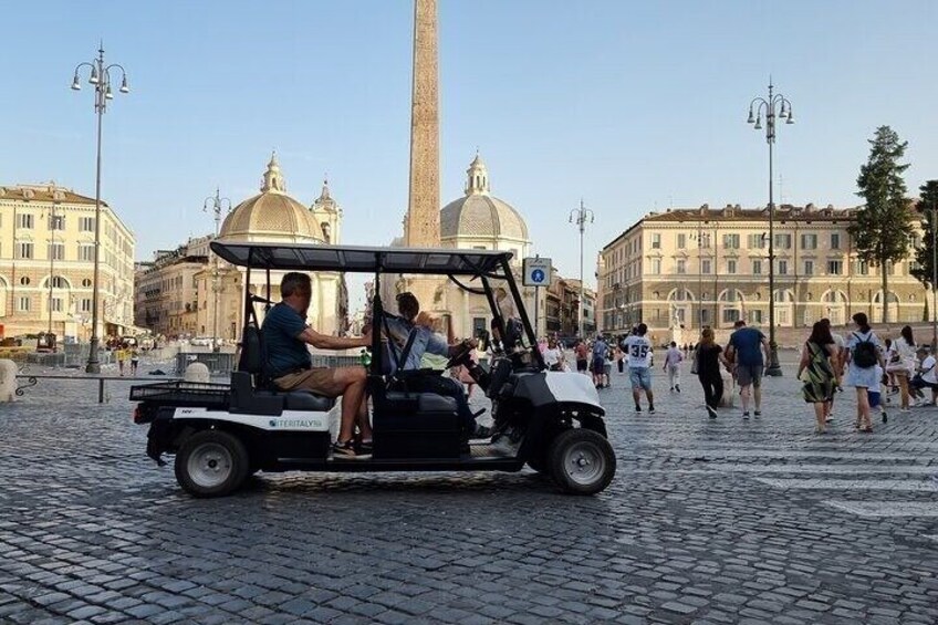 Un carrito de golf en una plaza adoquinada con turistas y edificios históricos al fondo. 3