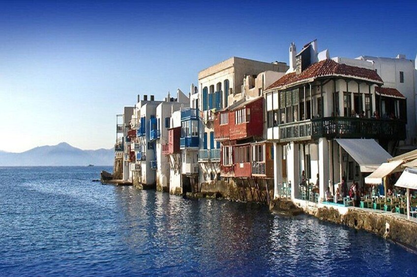 A coastal town with colorful buildings, a clear blue sea, and mountains in the background. 1
