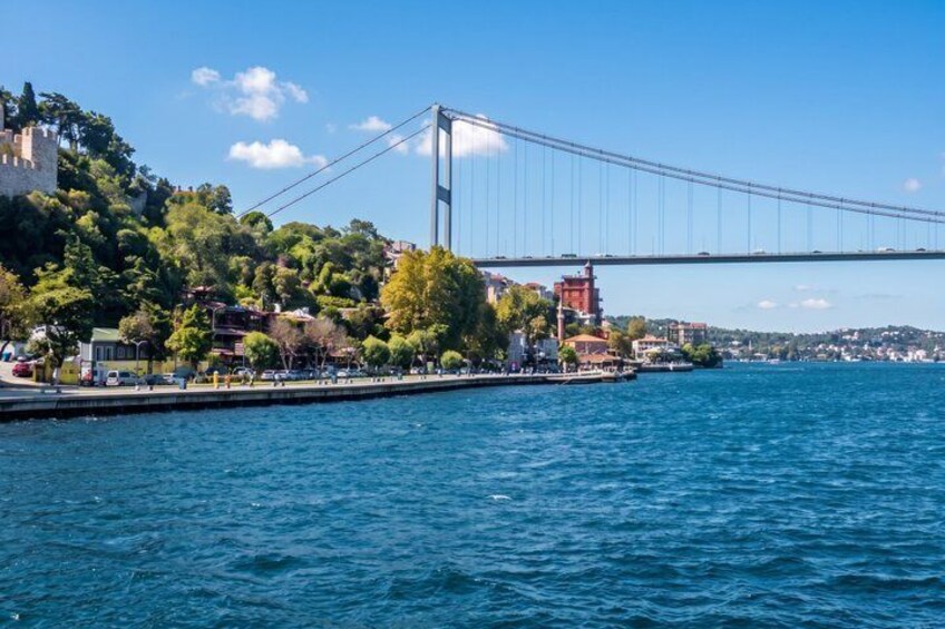 Eine Brücke überspannt ein Gewässer, im Hintergrund eine Hügelkette und Gebäude. 3