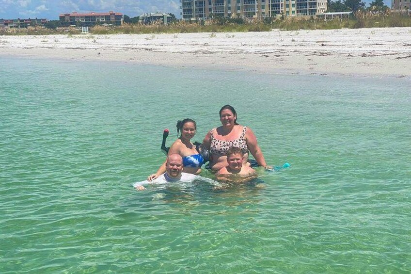 Three people in shallow water with a beach and buildings in the background. 2