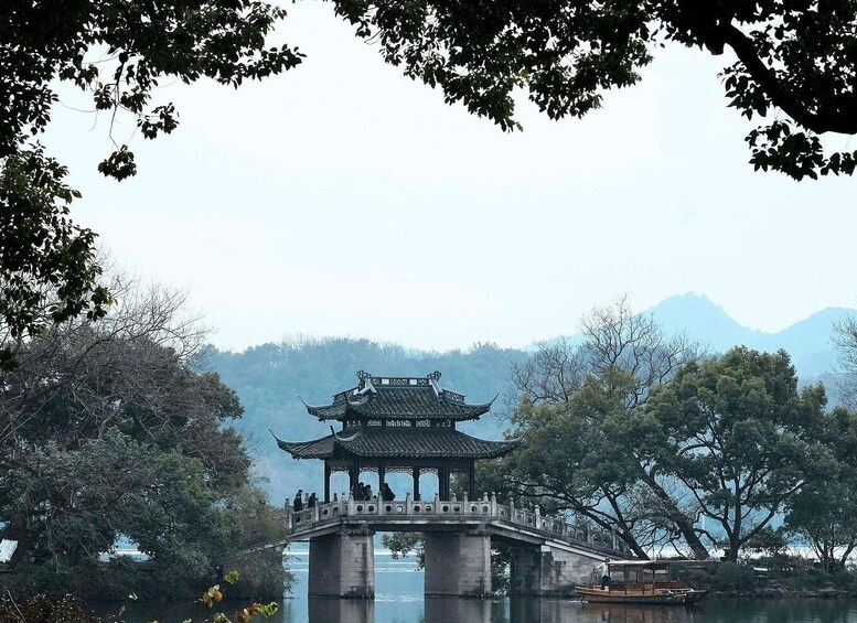 A traditional Chinese pavilion on a bridge over water, surrounded by trees and mountains. 1
