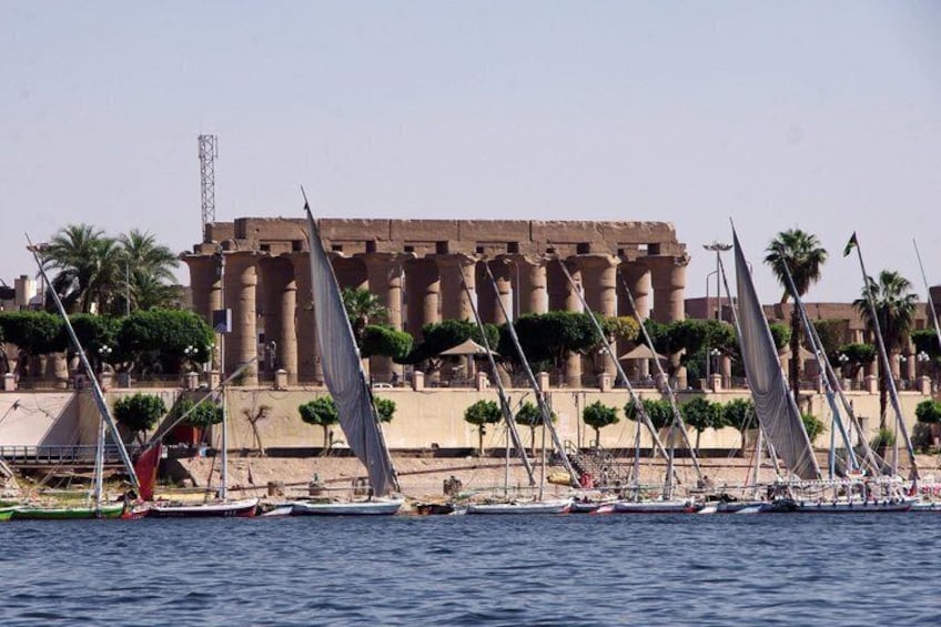 Un plan d’eau où l’on aperçoit des voiliers, des palmiers et, au loin, des exemples d’architecture de l’Égypte ancienne. 5