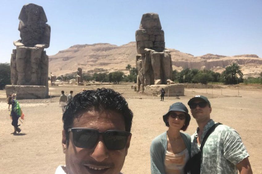 Paisaje desértico con grandes estatuas de piedra y pirámides al fondo. 4