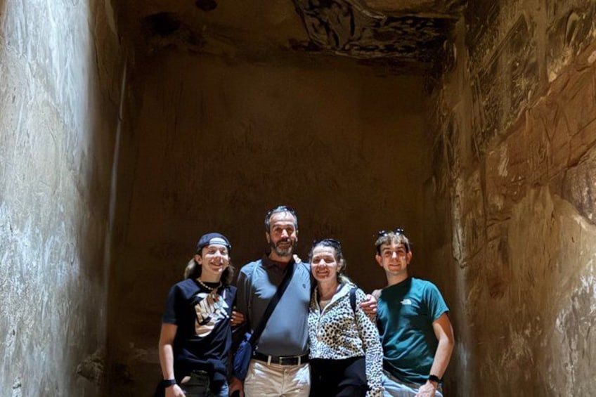 Un grupo de personas de pie en un estrecho pasillo de paredes de piedra con textura rugosa y techo ornamentado. 3