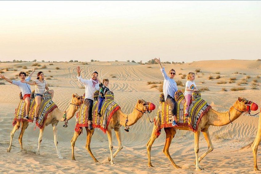 A group of people riding camels across a desert landscape with sand dunes in the background. 5