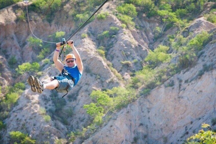 A person zip-lining through a canyon with rocky cliffs and sparse vegetation. 4