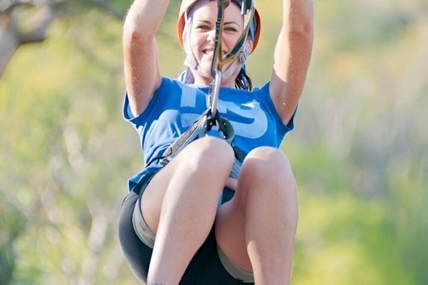 A person zip-lining with a harness and helmet, surrounded by greenery. 1