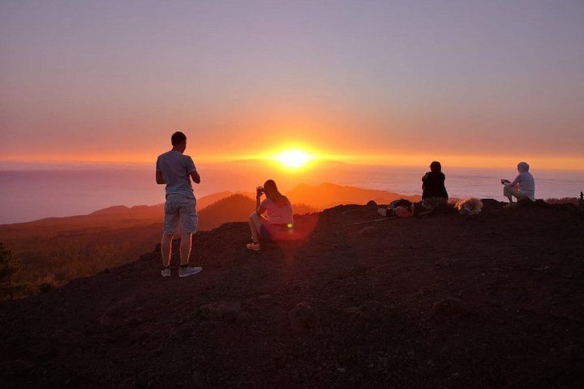 A sunset over a mountainous landscape with people sitting and standing on a hill. 5
