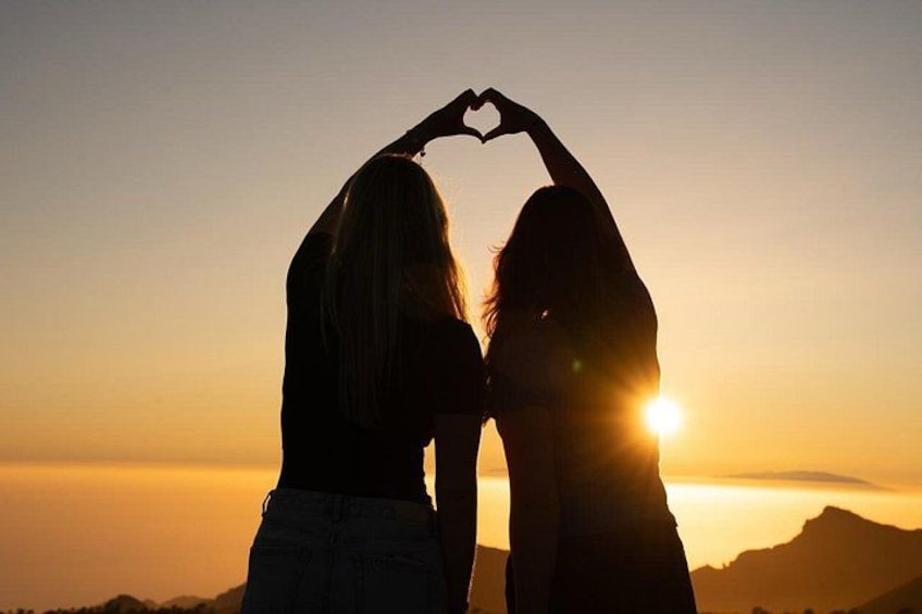 Two people forming a heart shape with their hands against a sunset background. 3