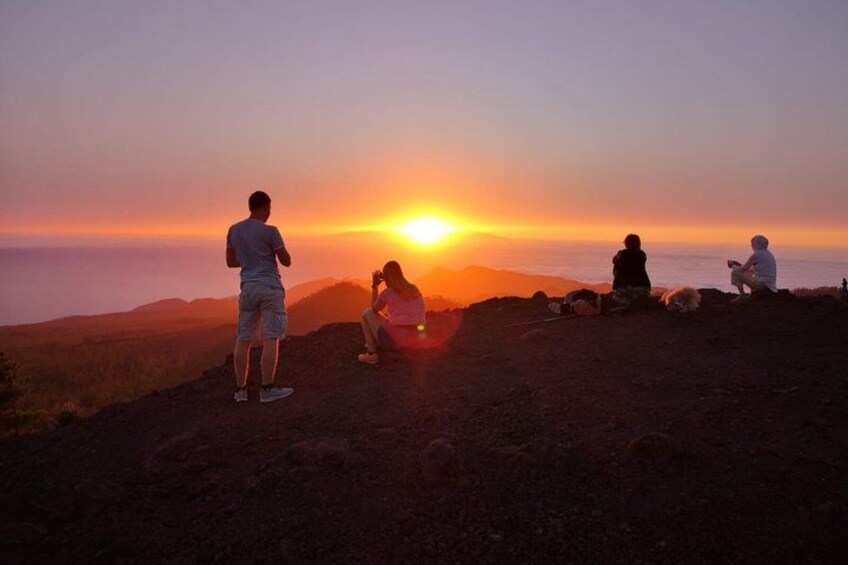 A sunset over a mountainous landscape with people sitting and standing on a hill. 5
