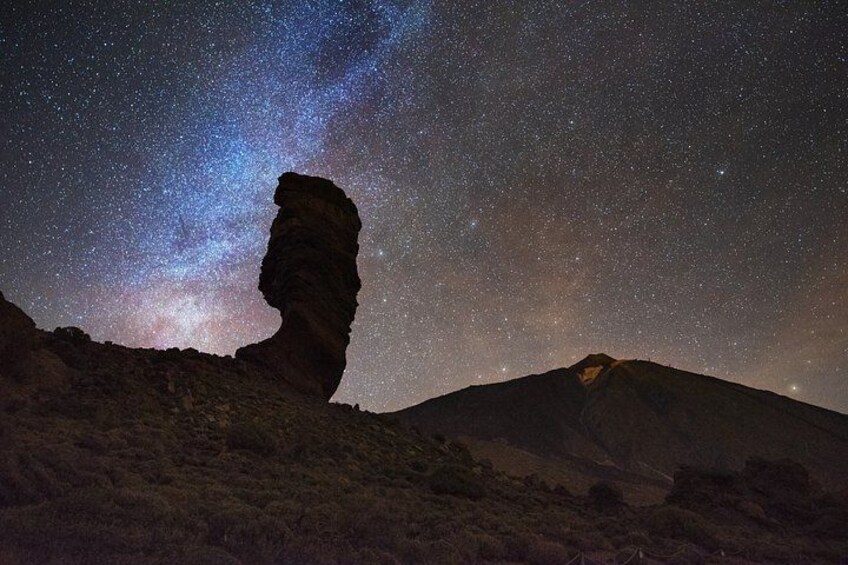 A starry night sky with a prominent rock formation in a desert landscape. 2