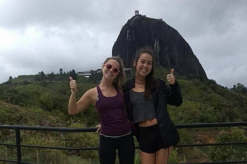 Two people giving thumbs up in front of a large rock formation. 2