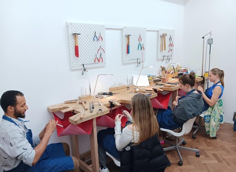 A jewelry workshop with tools and materials on tables, a pegboard with pliers, and people working. 3