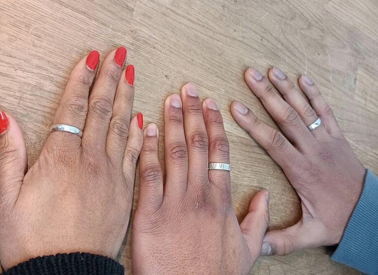 Four hands with red nail polish and silver rings on a wooden surface. 5