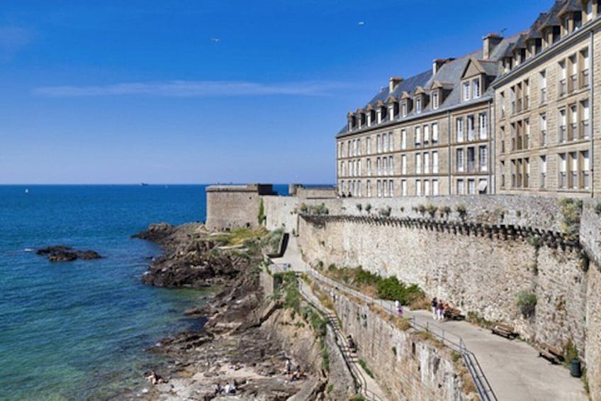 A coastal fortification with a stone wall, a paved walkway, and a building with multiple windows. 3