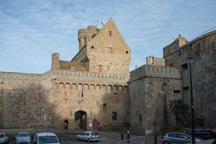 A historic stone castle with a prominent tower, arched entrance, and flags. 2
