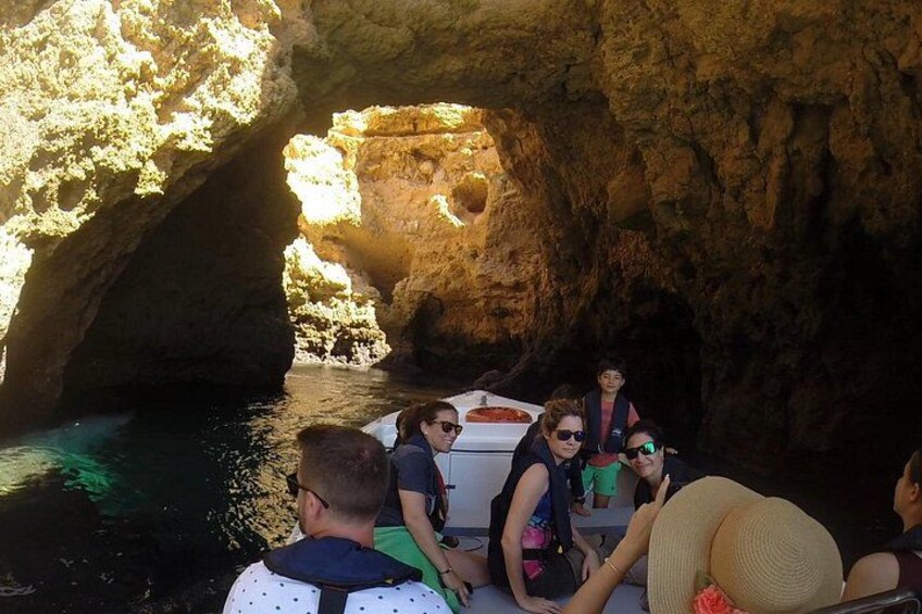 A group of people on a boat near a rocky cave entrance with water. 5