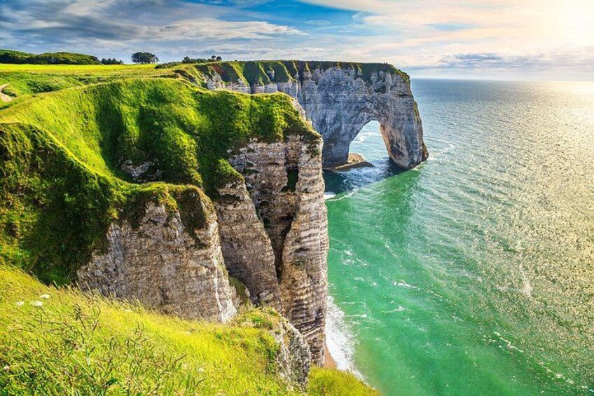 Eine Küstenklippe mit einer natürlichen Felsbrücke, grünem Gras und freiem Blick auf das Meer. 5